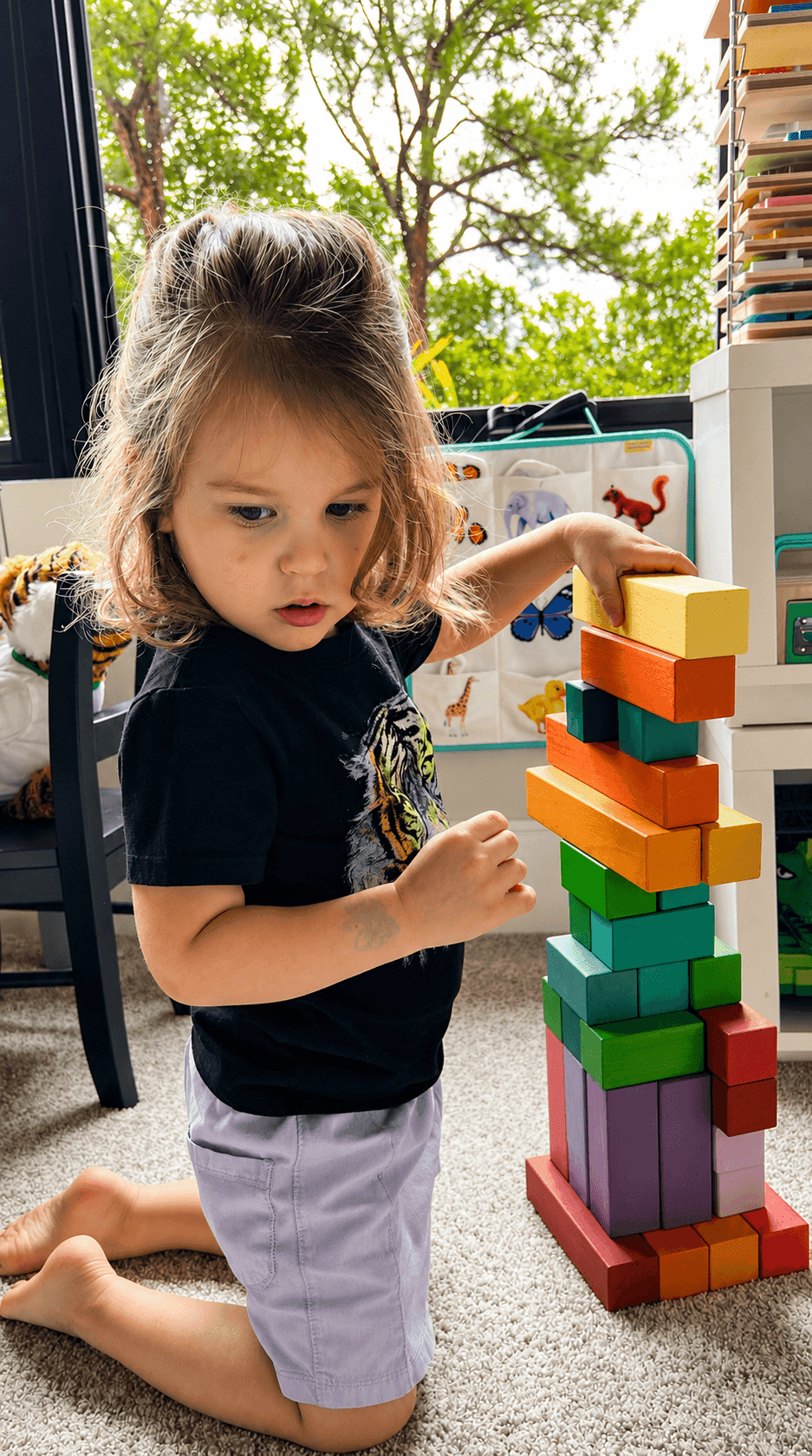 A child stacking a rainbow wooden block tower